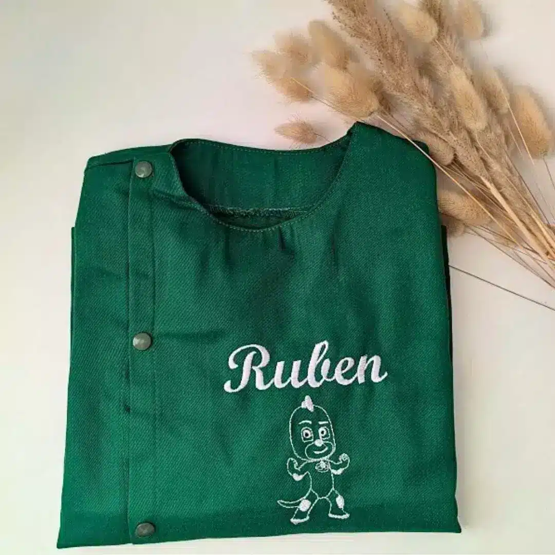 tablier maternelle vert personnalisé (1) Tablier en tissus pour école maternelle couleur vert modèle manches longues pour garçon brodé du prénom et d'un petit dessin en blanc