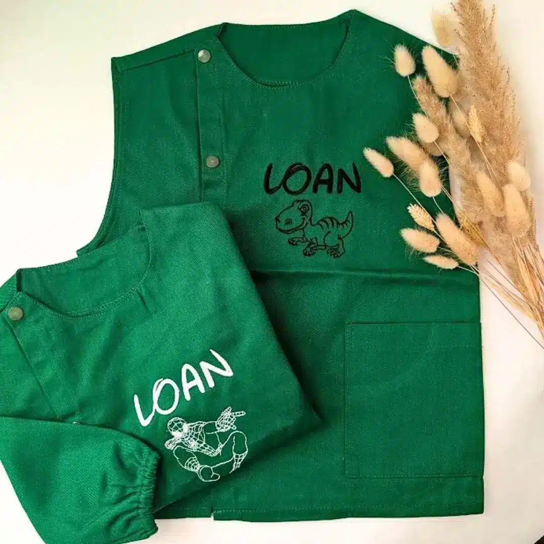 tablier maternelle vert personnalisé (2) Tablier en tissus pour école maternelle couleur vert modèle manches longues et sans manche pour garçon brodé du prénom Loan en blanc
