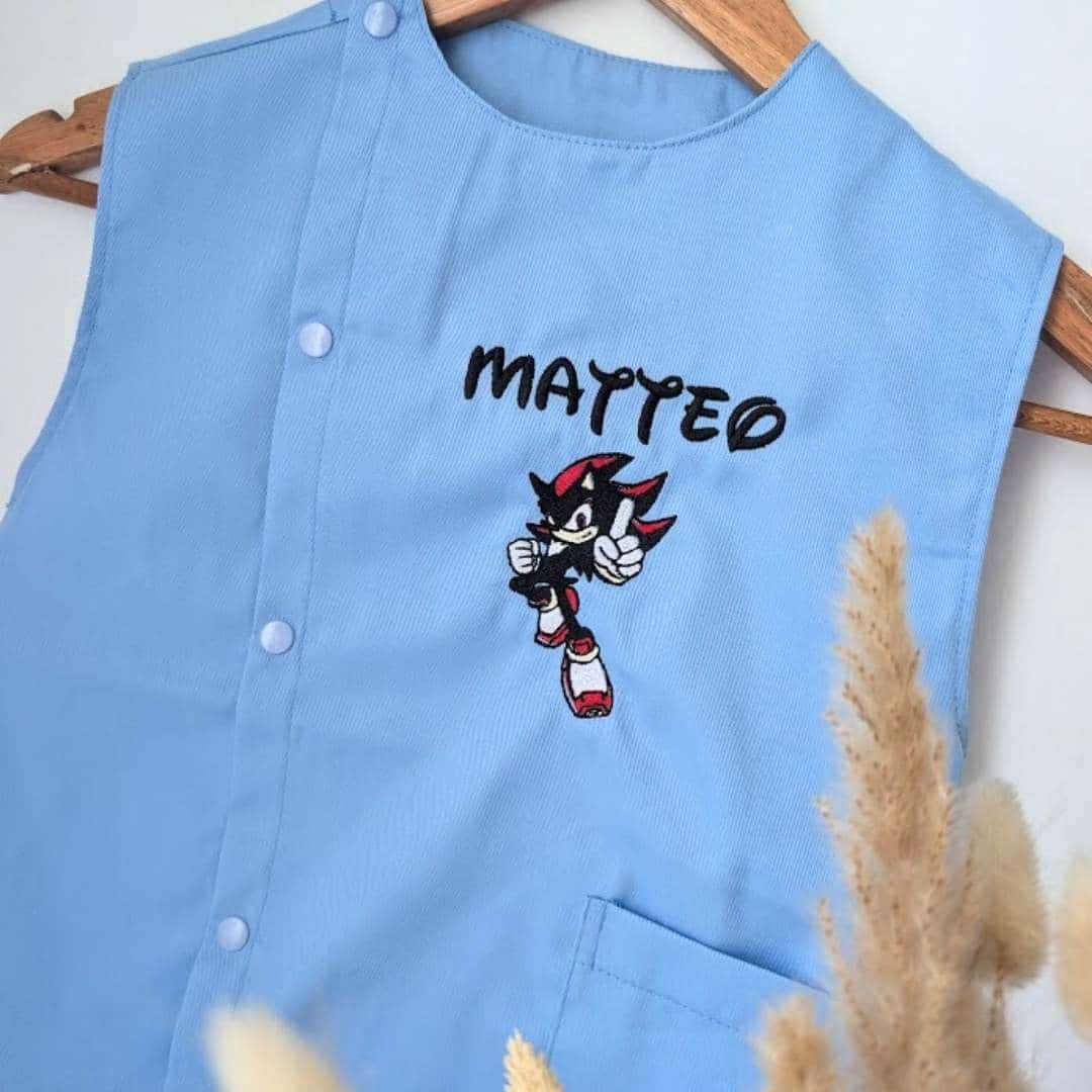 Tablier en tissus pour école maternelle couleur bleu modèle sans manches pour garçon brodé du prénom Matteo en noir