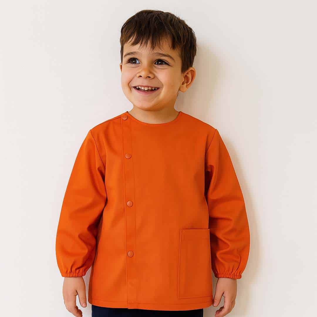 Petit garcon portant un tablier en tissus manche longue orange pour la maternelle brodé de son prénom