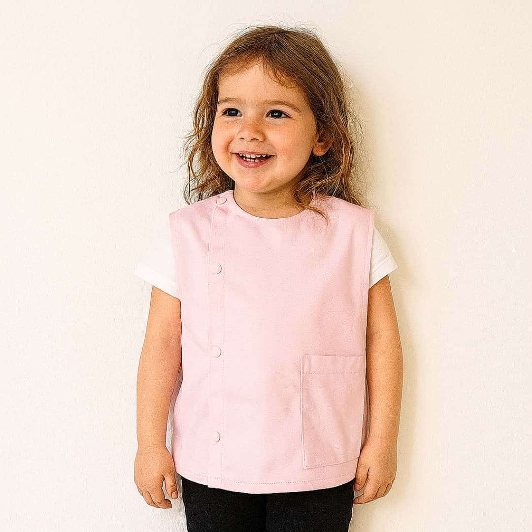 Petite fille portant un tablier en tissus manche courte rose pour la maternelle brodé de son prénom
