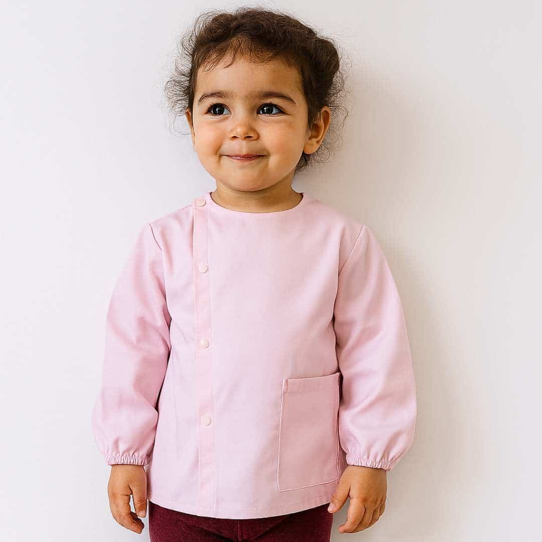 tABLIER ROSE MATERNELLE Petite fille portant un tablier en tissus manche longue rose pour la maternelle brodé de son prénom