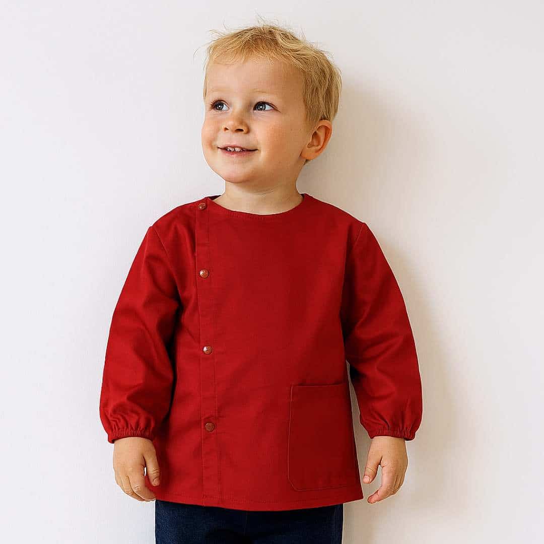 Petit garcon portant un tablier en tissus manche longue rouge pour la maternelle brodé de son prénom