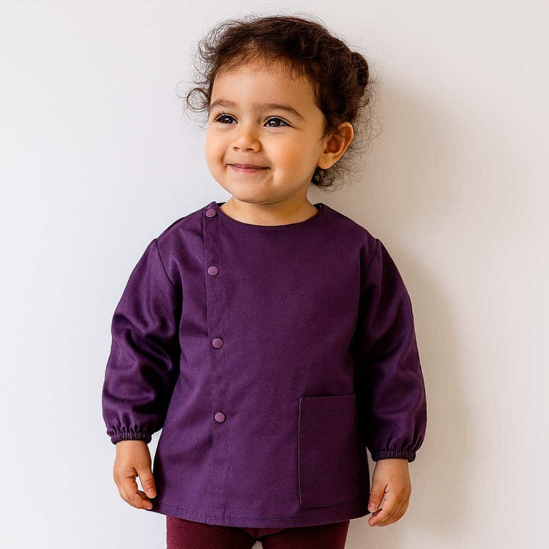 Petite fille portant un tablier en tissus manche longue violet pour la maternelle brodé de son prénom